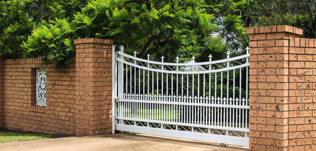 White wrought iron driveway entrance gates in brick fence